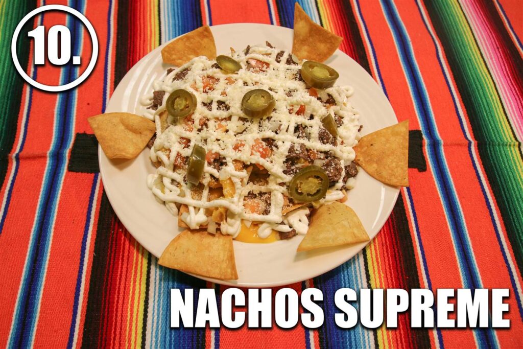 A plate of nachos with sour cream, cheese and jalapenos.